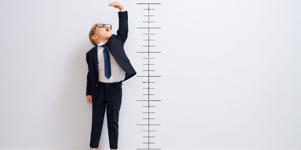 Little child is playing businessman. Kid is measuring the growth on the background of wall. Smart power concept.